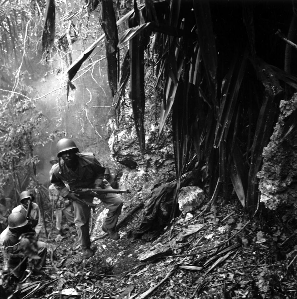 March 10, 1945: U.S. troops in the Pacific islands continued to find enemy holdouts long after the main Japanese forces had either surrendered or disappeared. Guam was considered cleared by August 12, 1944, but parts of the island were still dangerous half a year later. Here, patrolling Marines pass a dead Japanese sniper. These Marines may belong to the Fifty-second Defense Battalion, one of two black units sent to the Pacific. (Charles P. Gorry, AP Staff/AP Archives)