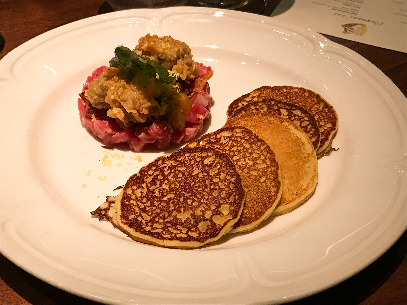 Beef Tartare served with two crispy fried oysters, pickled gooseberry, celery root remoulade, and corn meal pancakes. Fixe Southern restaurant in Austin Texas